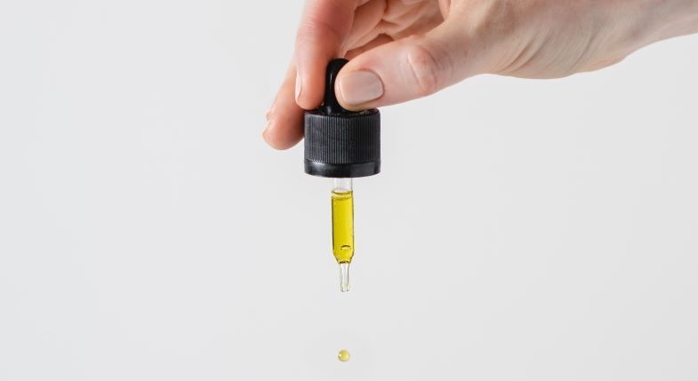 Gotas de aceite de CBD cayendo de una pipeta de cristal sobre fondo claro