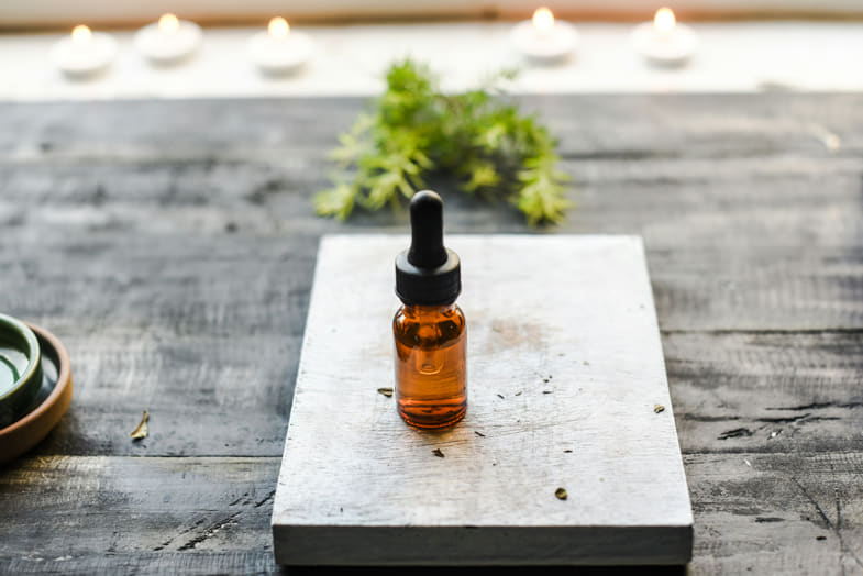 frasco de aceite de CBD sobre una mesita de madera con hojas de cannabis ligeramente difuminadas al fondo